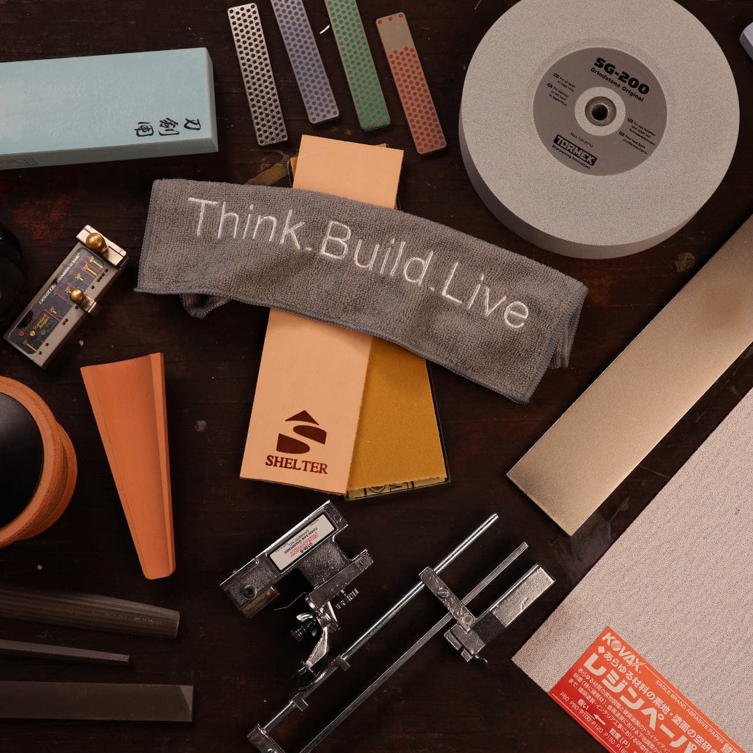 A collection of woodworking and sharpening tools, stones, rulers, and a cloth with the text “Think. Build. Live.” displayed on a wooden surface—perfect for any Shelter Institute or timber framing tools enthusiast.
