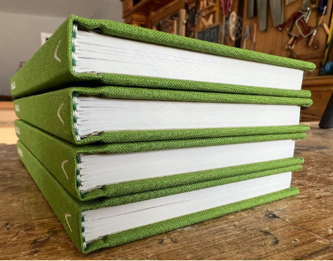 A single green hardcover book titled “Smalls: 18 Well-designed, Easy Projects for an Afternoon in the Workshop” by Shelter Institute rests horizontally on a wooden surface, its spine facing left. Shelves with tools and woodworking projects can be seen in the background.