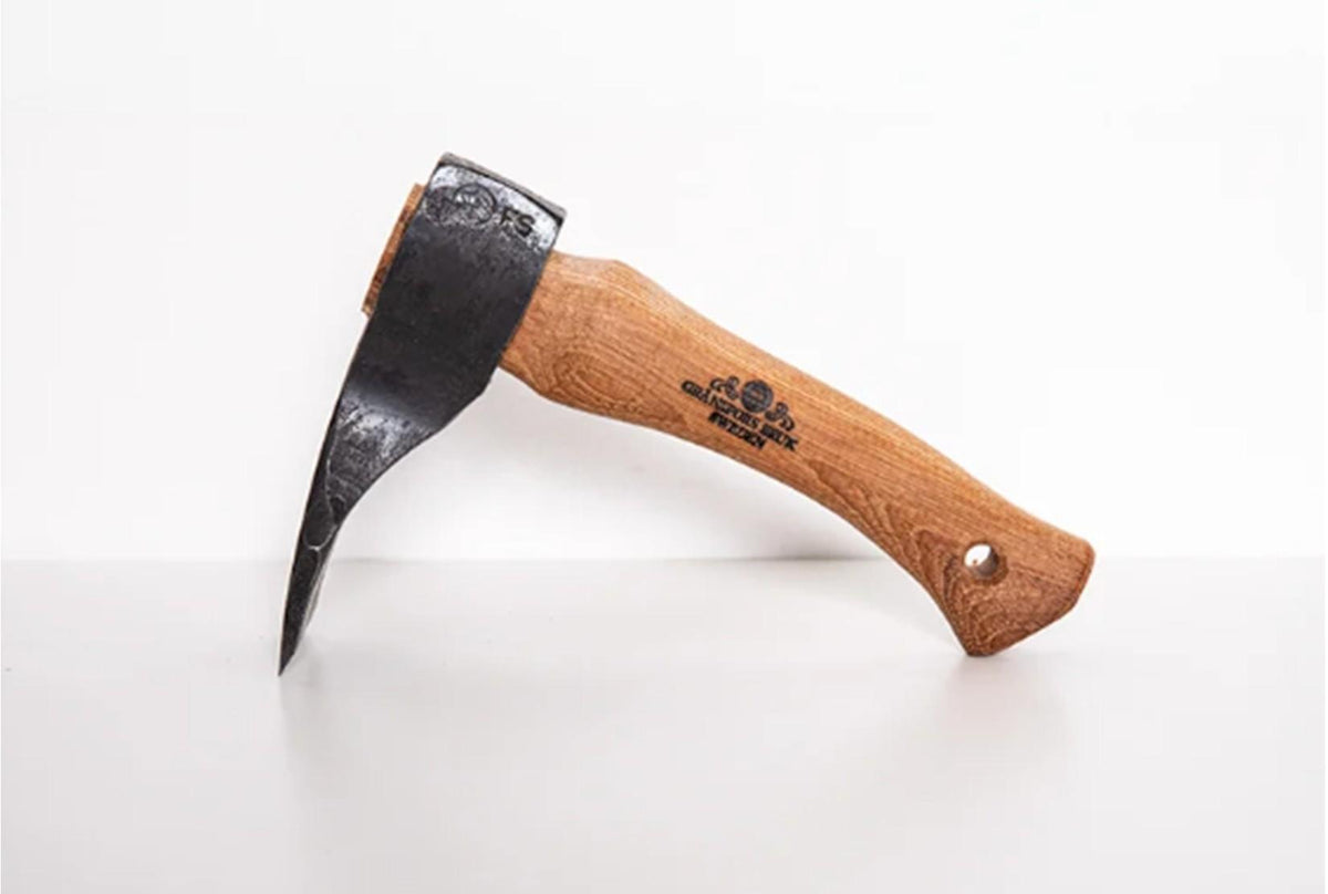 A Shelter Institute Small Straight Adze 56mm with a wooden handle and a black metal head, featuring a straight, sharp blade for precision shaping, is resting on a light-colored surface. Its sturdy design is reminiscent of tools from Gränsfors Bruk, often used in traditional log building for reliable performance and accuracy.