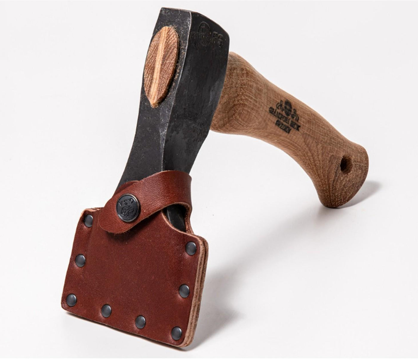 Shelter Institute’s Small Straight Adze 56mm features a finely crafted wooden handle and a black blade, accompanied by a brown leather sheath secured with metal rivets. Photographed on a plain white background, this tool is an ideal companion for log building or woodworking tasks, reminiscent of the quality found in Gränsfors Bruk tools.