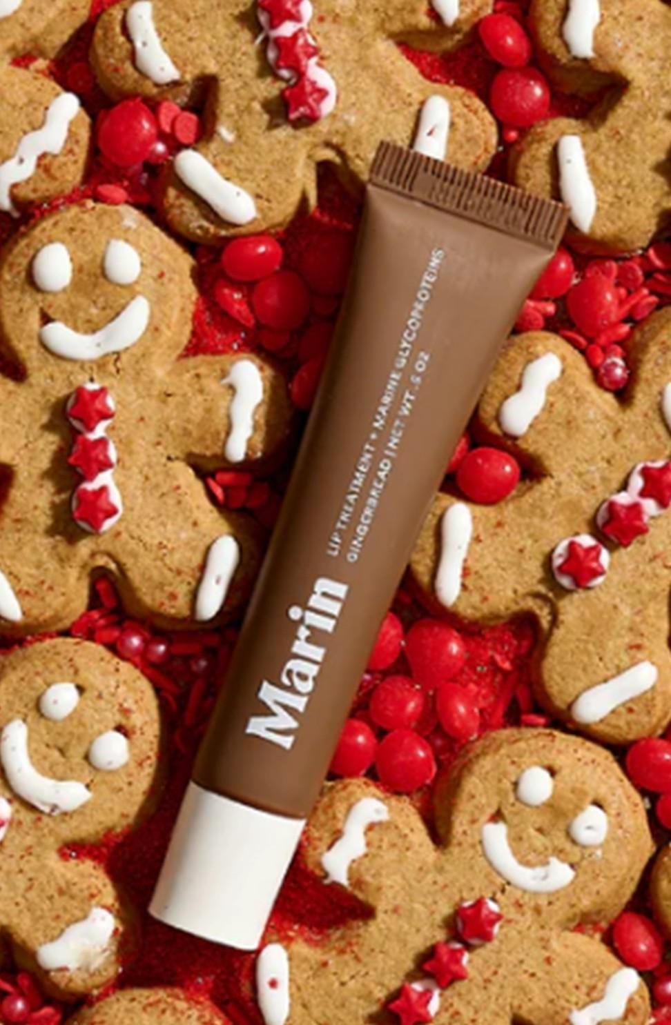 A Marin Lip Treatment tube rests on gingerbread cookies topped with white icing, surrounded by red candies.