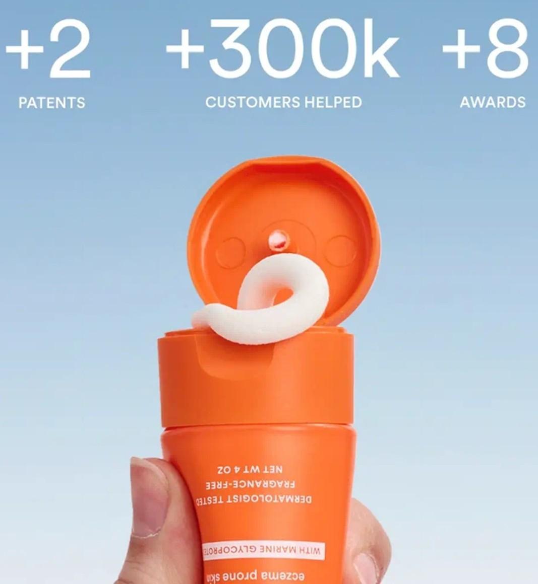 A hand holds Marin Soothing Hydration Cream as white cream dispenses from the orange bottle. Text above: +2 patents, 300k+ customers helped, 8+ awards. Features Marine Glycoproteins for advanced skin barrier repair on a light blue background.