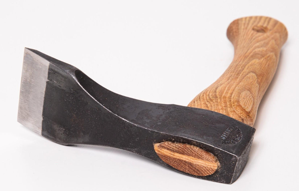 A close-up of a Shelter Institute Small Straight Adze 56mm featuring a sharp, wide metal blade and a smooth, curved wooden handle, photographed on a white background—an essential tool for log building.