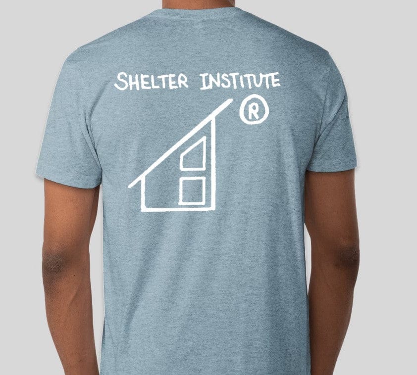 Back view of a person in a gray Custom Ink 50th Anniversary Adult T-Shirt featuring "Shelter Institute" and a white house logo on the back, celebrating 50 years of building knowledge.