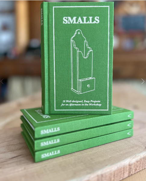 A stack of four green hardcover books titled Smalls: 18 Well-designed, Easy Projects for an Afternoon in the Workshop from Shelter Institute, each featuring a white line drawing of a woodworking project on the cover, rests on a wooden surface like an inviting pocketbook for woodworking enthusiasts.