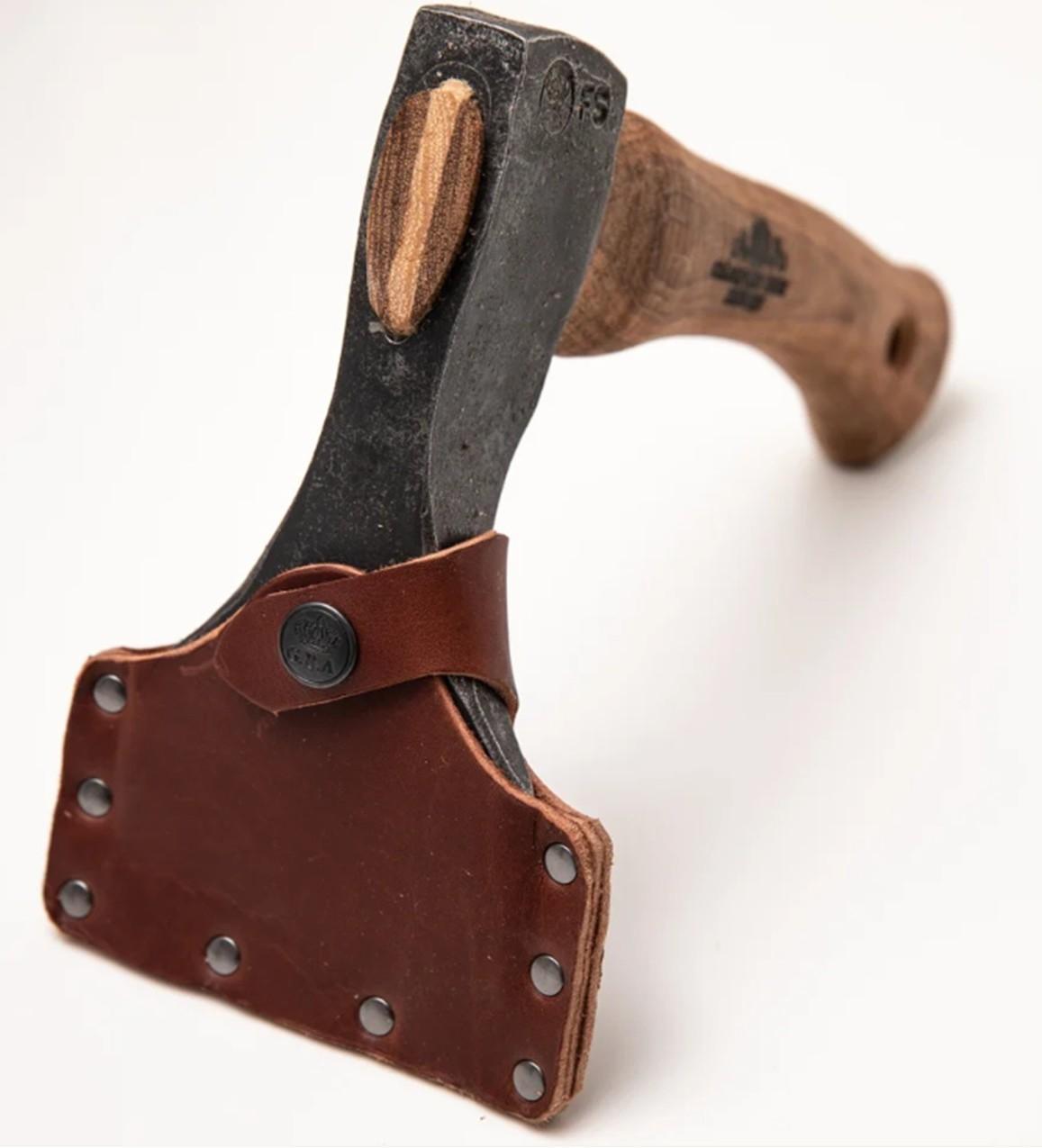 A Gransfors Bruks Small Straight Adze 80 mm, featuring a wooden handle and a leather sheath covering the blade, designed for log building tasks, is shown on a plain white background.