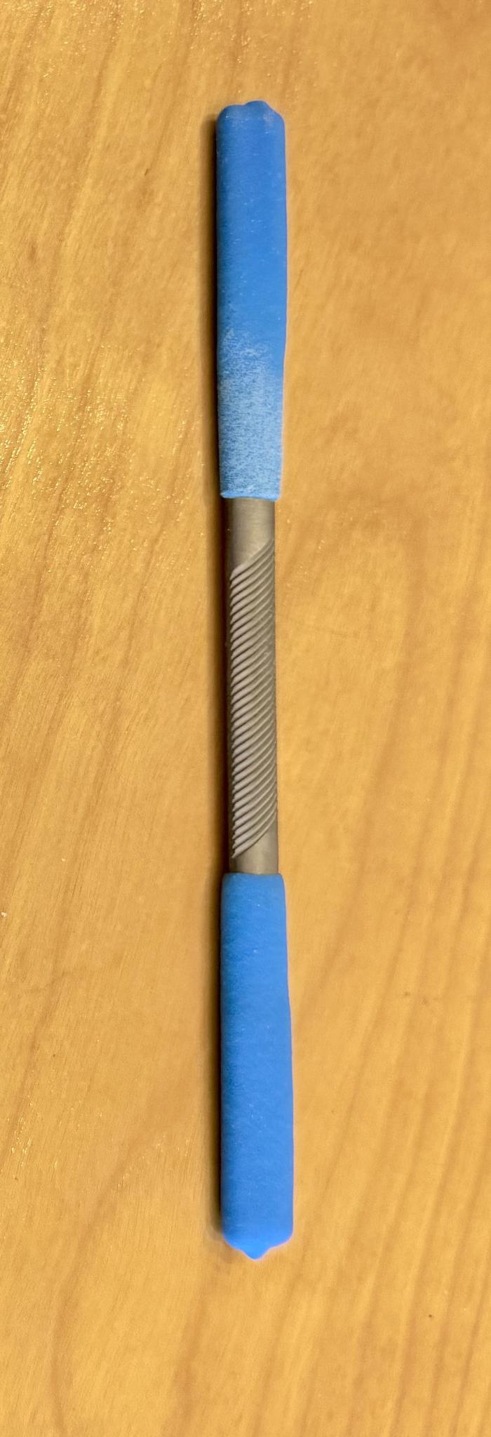The Iwasaki Draw File by Iwasaki is a metal tool with a textured center grip and blue foam ends, perfect for wood carving and creating smooth finishes. It is shown resting on a wooden surface.