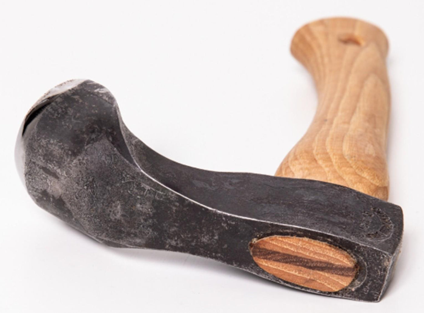 A hammer with a severely bent wooden handle and a black metal head, photographed on a white background, evokes the well-worn tools often found in traditional log building or alongside specialized implements like the Gransfors Bruk Small Gutter Adze Radius 25, Second Grade.