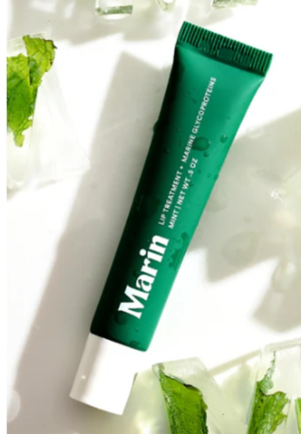 A green tube of Marin Lip Treatment by Marin, with a white cap, rests on a white surface among ice cubes and mint leaves—featuring marine glycoproteins for enhanced moisture in your lip care routine.