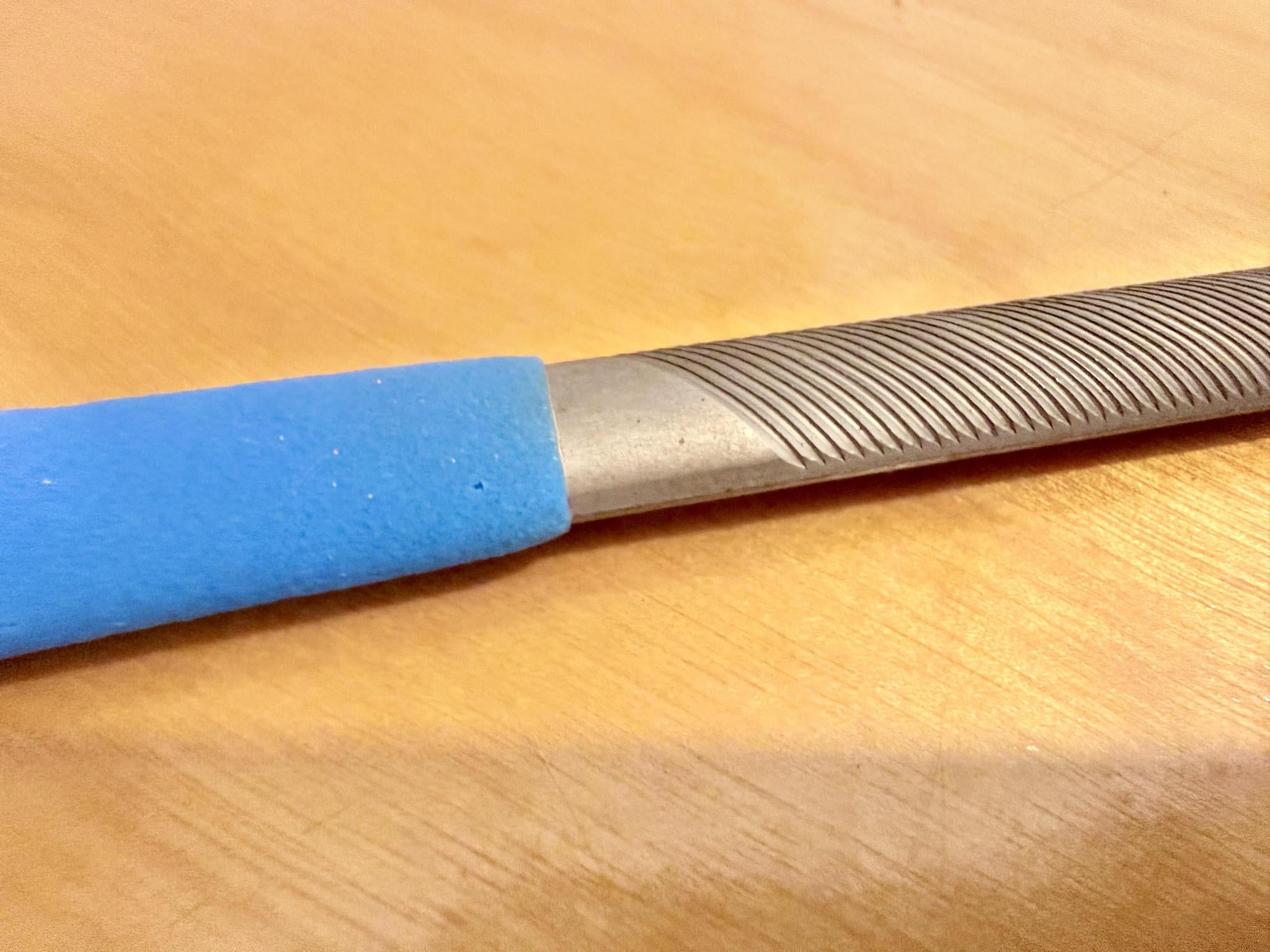 Close-up of the Iwasaki Draw File by Iwasaki, featuring a textured grooved surface and blue handle on light wood—perfect for wood carving and producing a smooth finish.