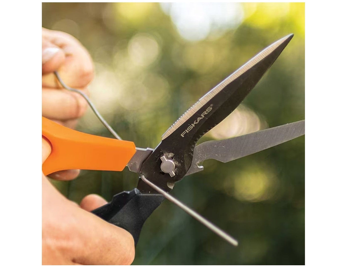 A close-up of hands sharpening FIS Multi Purpose Garden Shears outdoors with a sharpening tool, highlighting precision-ground steel blades against a blurred green background.