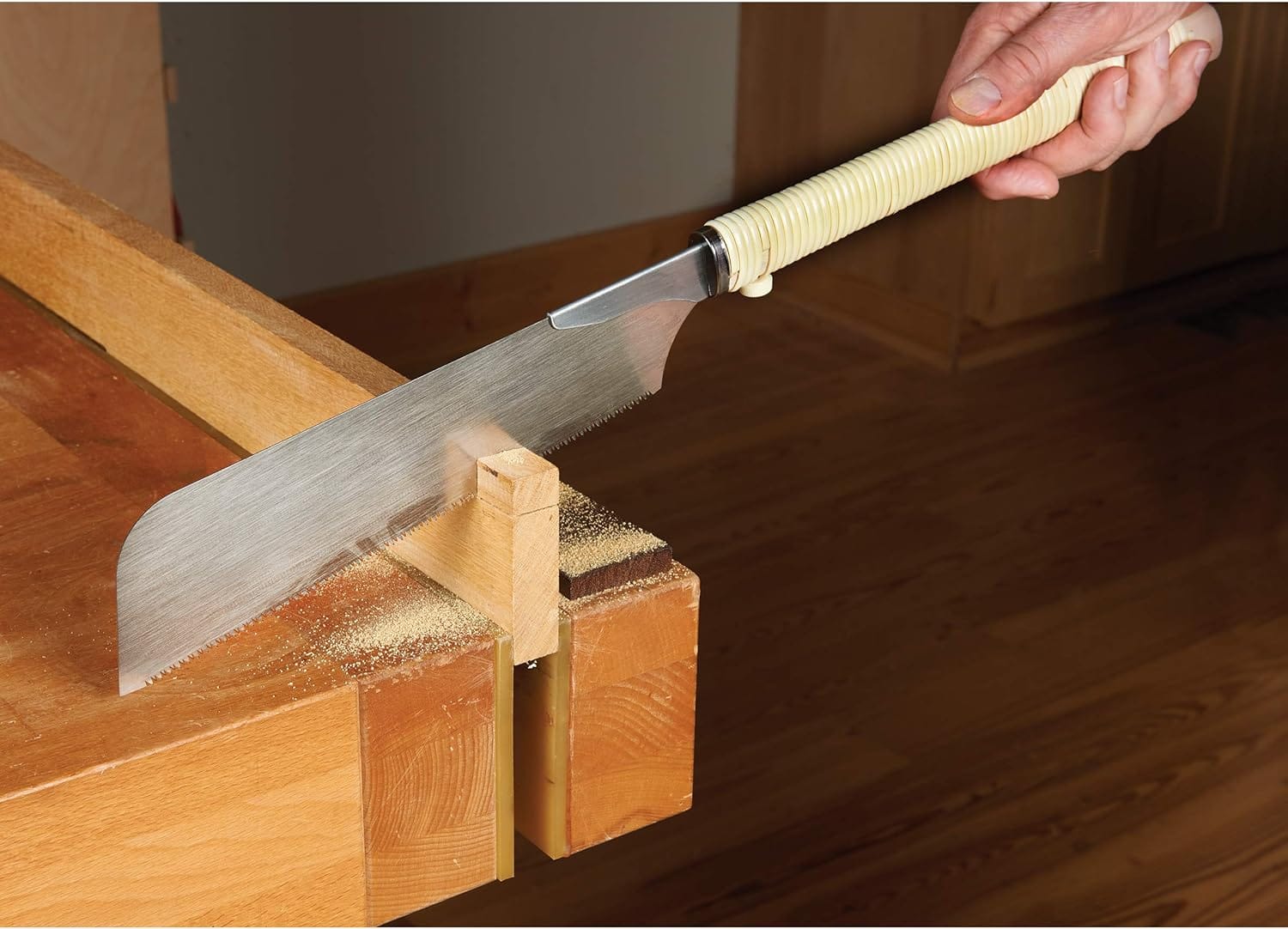 A person uses a BBT Gyokucho Crosscut Razorsaw No. S-400 with a 240mm blade to cut wood clamped to a workbench, as woodworking shavings collect below the cut.