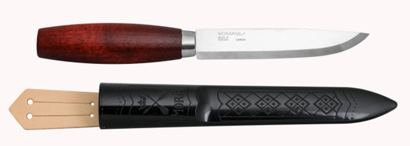 The Classic Mora Knife by Industrial Revolution features a high-carbon steel blade, a birch wood handle, and is displayed with an intricately carved black sheath.