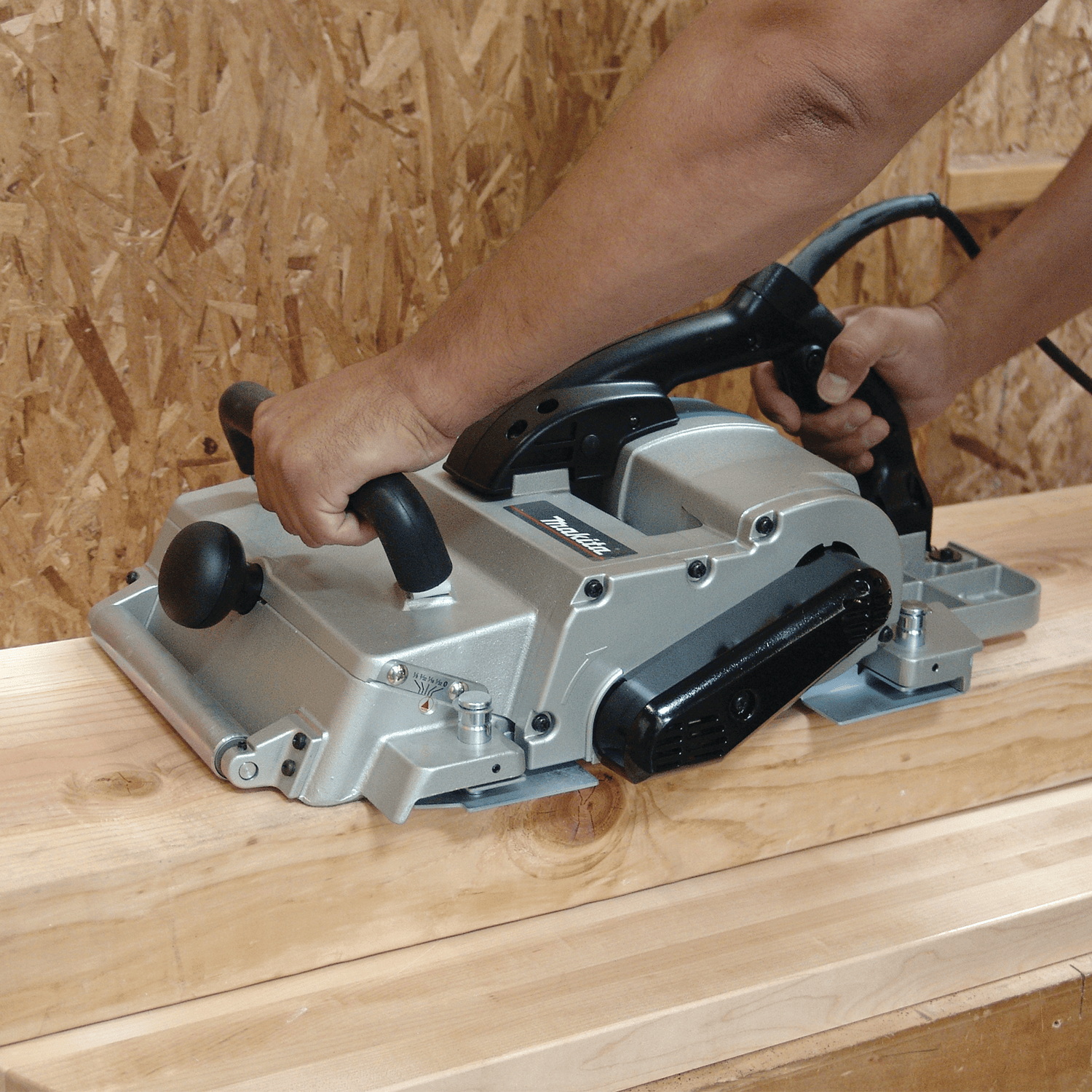 A person uses the Makita 12-1/4-in Planer in a wooden workshop, smoothing a beam efficiently with its powerful 15 AMP motor for precise results.