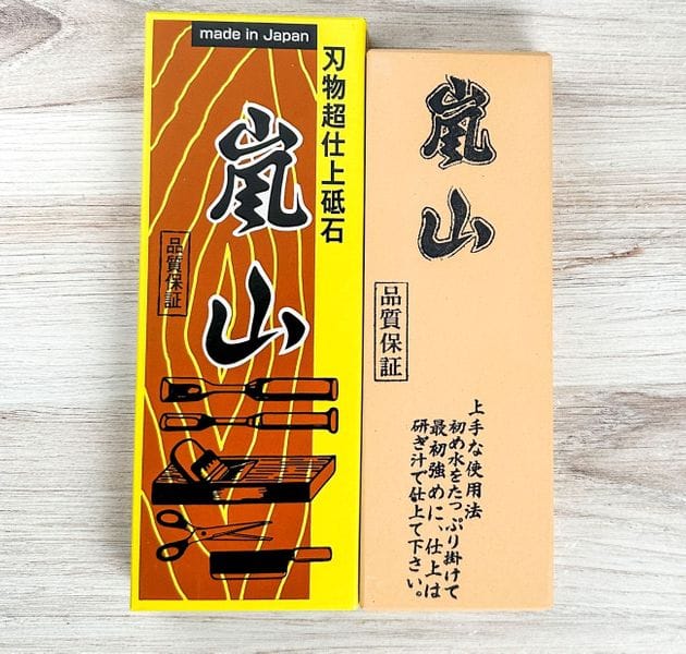The MARU Arashiyama Sharpening Stone is a rectangular Japanese 6000 grit water stone in brown, yellow, and beige with bold Japanese characters, wood grain patterns, and a “Made in Japan” label—ideal for kitchen knives.