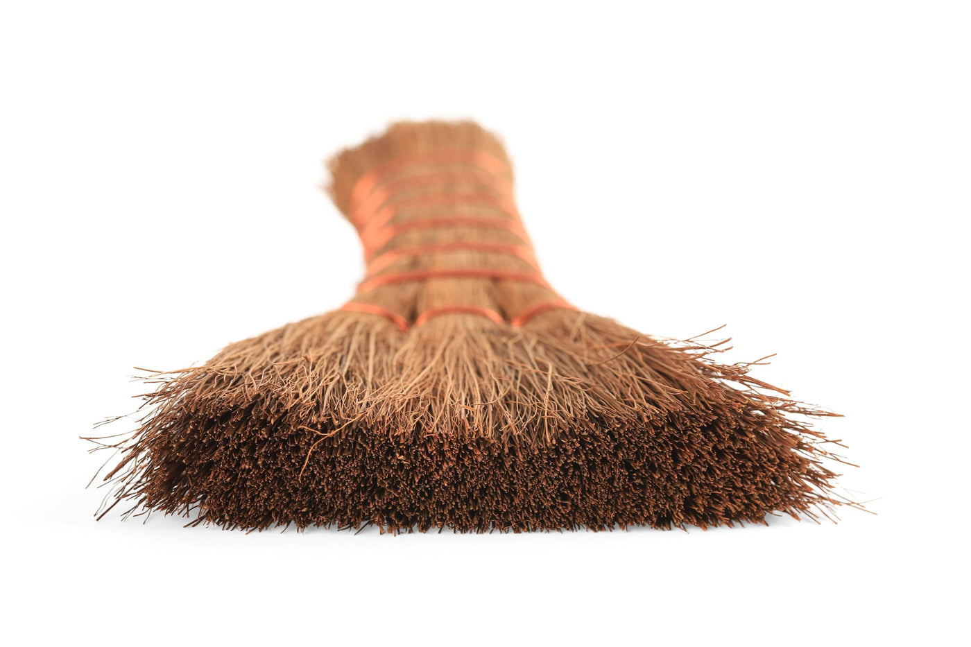 A close-up of the MARU Japanese Natural Bristle Hand Broom shows its densely packed natural bristles, reminiscent of a traditional straw broom, bound with vibrant red twine.