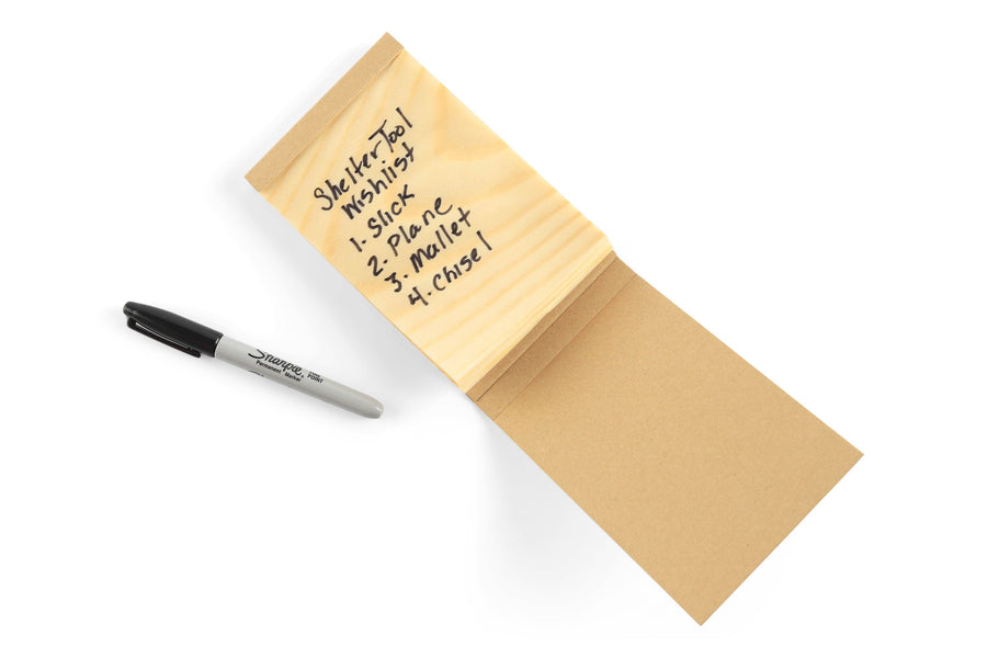 A Sharpie marker lies next to a MARU Kyougi Wooden Notepad, renowned for its traditional Japanese craftsmanship and sustainable forestry practices, with a Shelter Tool Wishlist listing sling, plane, mallet, and chisel.