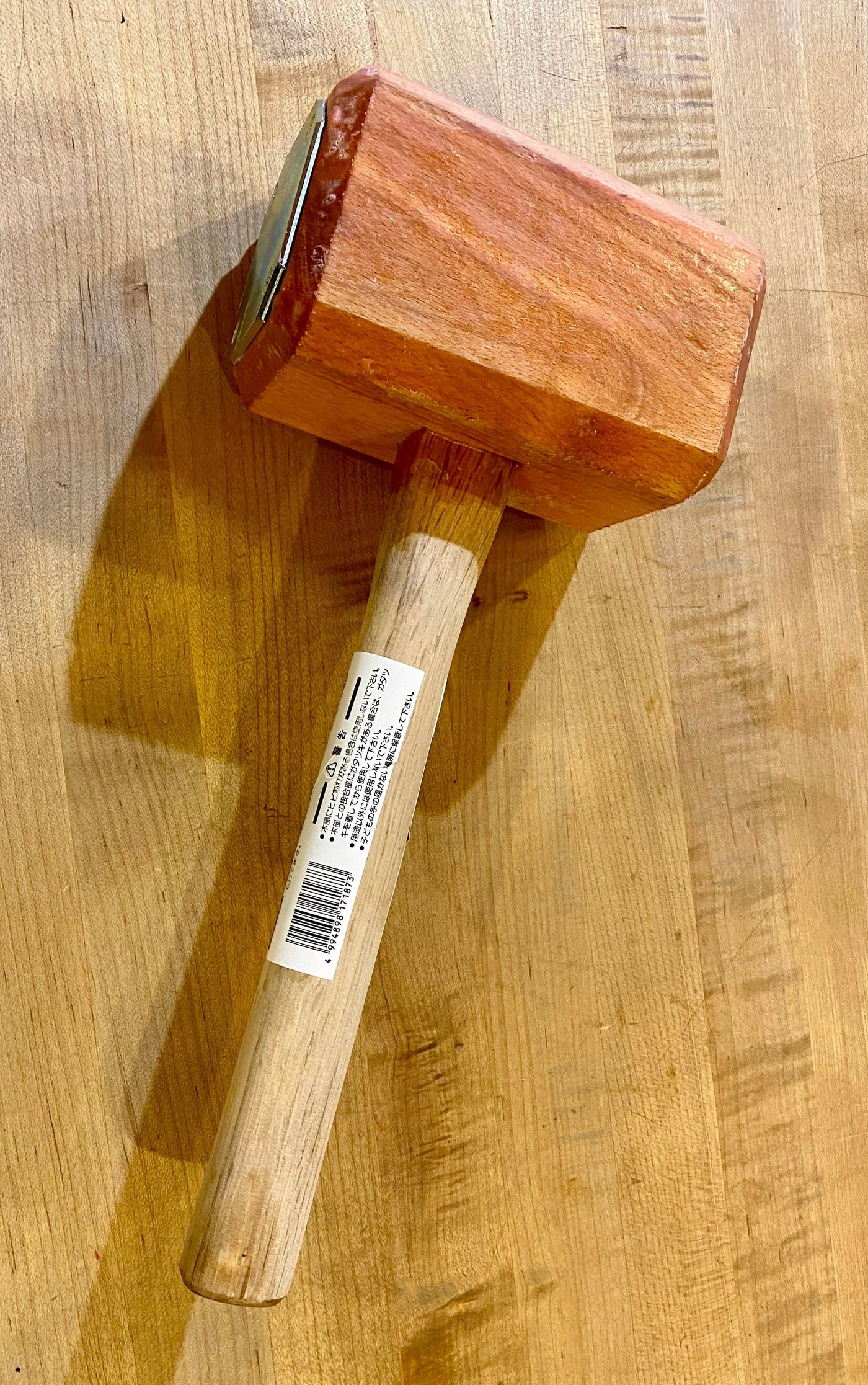 The MARU Iron-Plated Wood Mallet, crafted from Japanese White Oak, has a rectangular head and long handle and rests elegantly on a wooden surface.