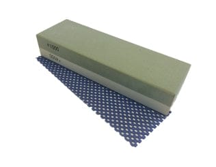 The MARU Imanishi Wetstone 1000/4000, a rectangular two-in-one whetstone, rests on a blue perforated mat, ready for sharpening tasks.