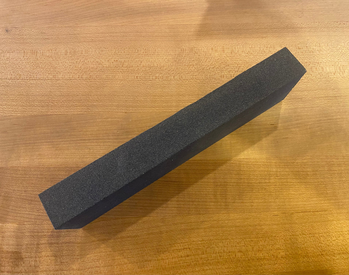 A long black foam block rests on a wooden surface alongside the MARU 180 Grit Japanese Water Stone, ready for precision reshaping tasks.