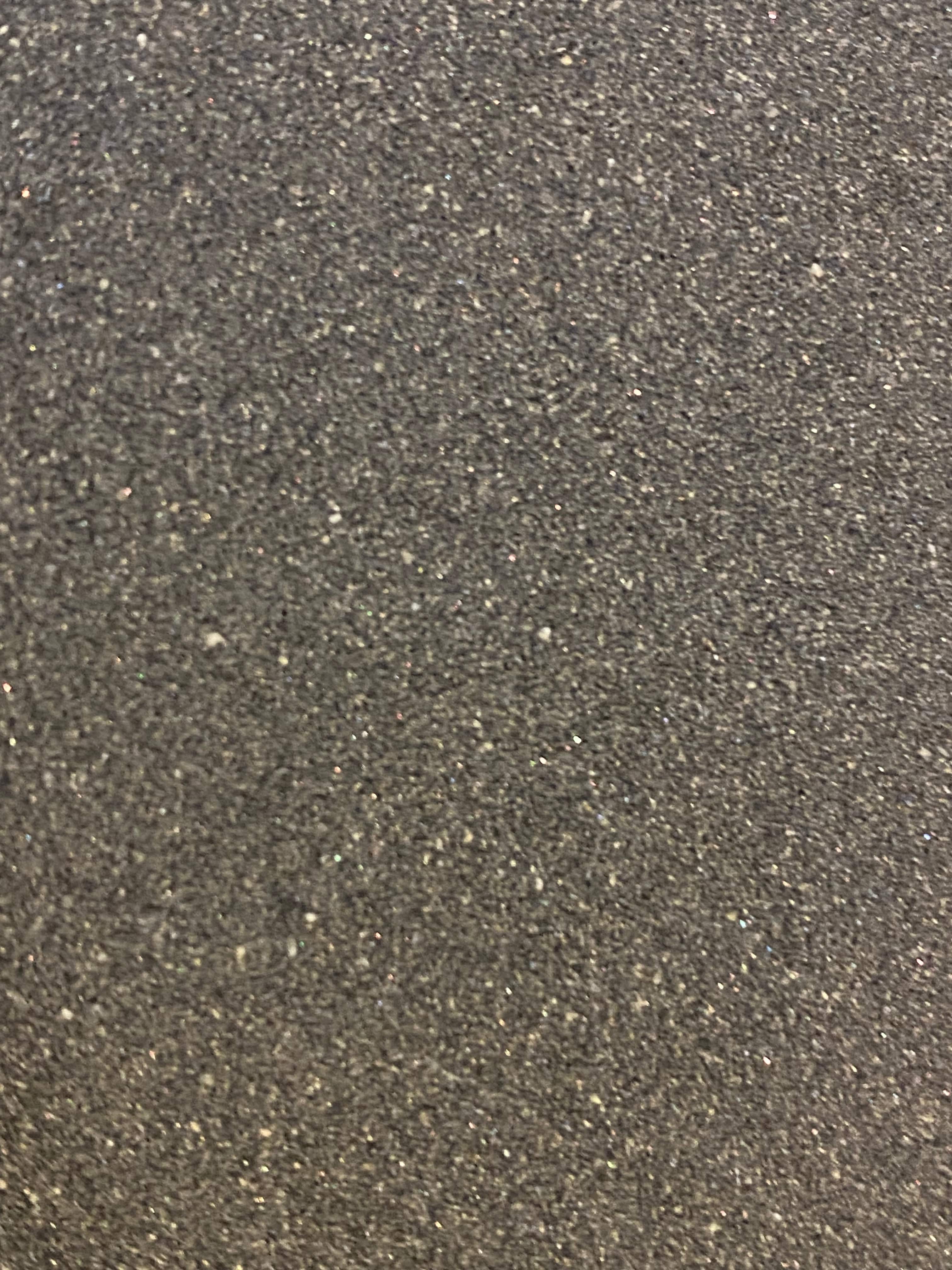 A close-up of a textured surface covered in gray and black speckles, reminiscent of the fine abrasion seen on the MARU 180 Grit Japanese Water Stone.