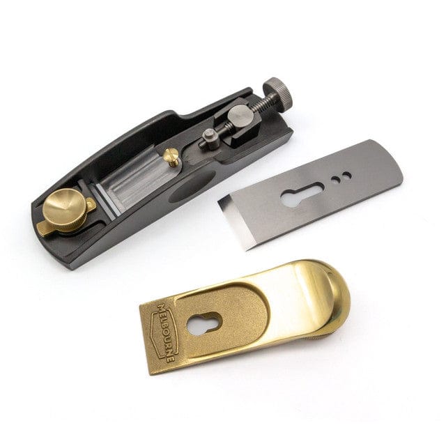 The Melbourne Tool Company Low Angle Block Plane by Melbourne Tool Company is shown disassembled on a white surface, featuring its black body, brass cap, and M2 High Speed Steel blade.