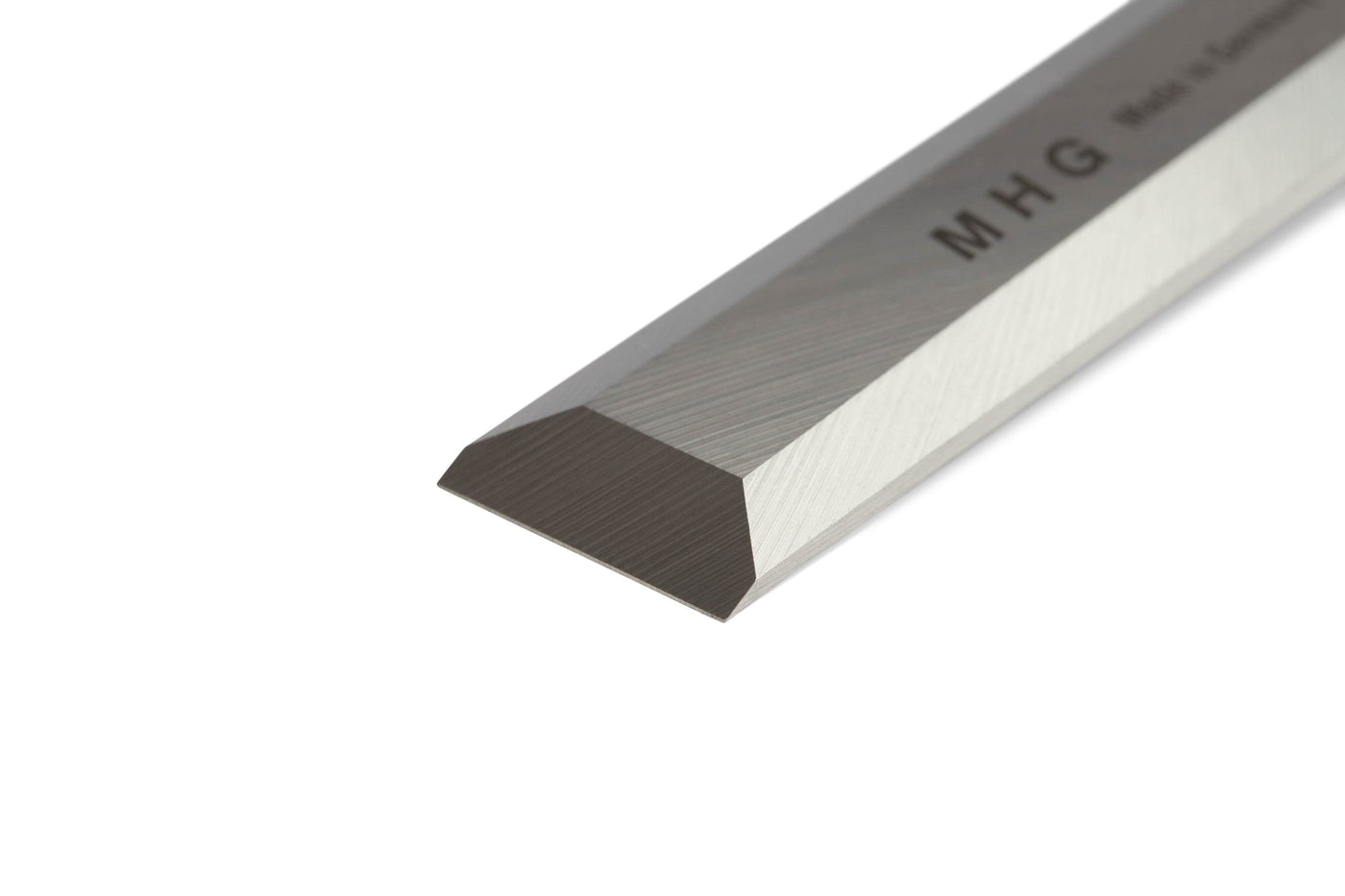 Close-up of the MHG Firmer Bench Chisel’s beveled steel blade, engraved with “MHG,” photographed on a white background—a premium tool for fine woodworking collections.