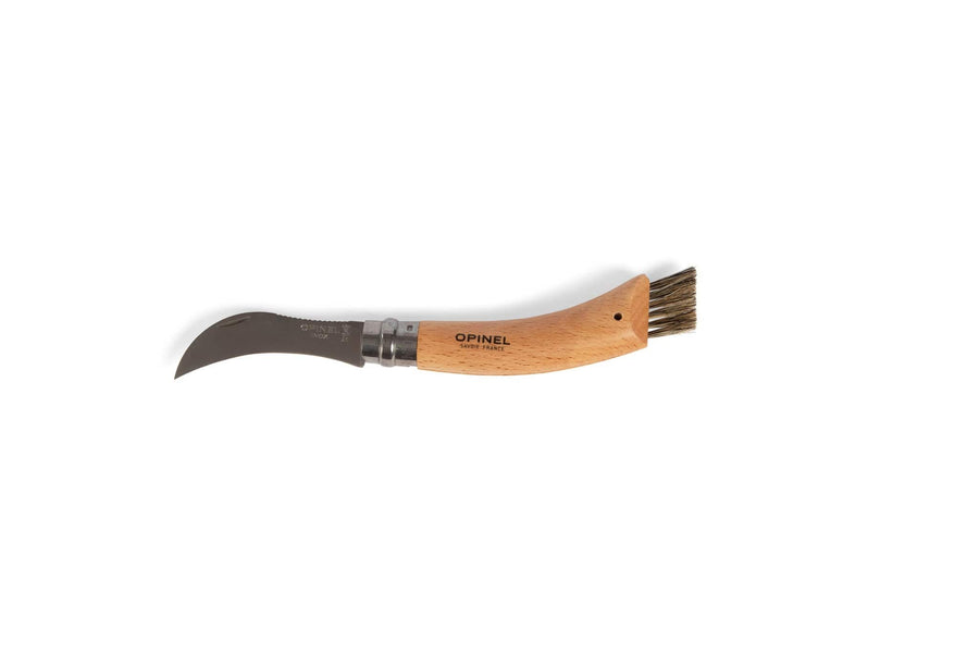The Opinel Mushroom Knife by Opinel features a short, curved stainless steel blade and a wooden handle with a boar bristle brush at the end, shown lying on a white background with the brand name visible on the handle.