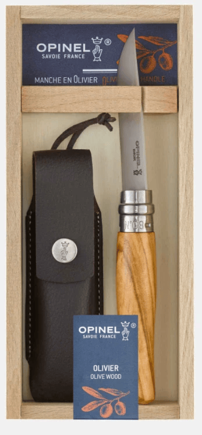 The Opinel No 08 Stainless Knife with Olive Wood Handle by Opinel is shown boxed beside a black synthetic leather sheath. The packaging displays the Opinel logo and olive branch artwork.