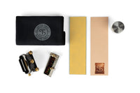 The Shelter Sharpening Kit by Shelter Institute, reminiscent of a woodworking toolset, includes tools such as a black cloth, two rectangular items, a cylindrical metal piece, a bridge-like component, and a gauge tool set against a white background.