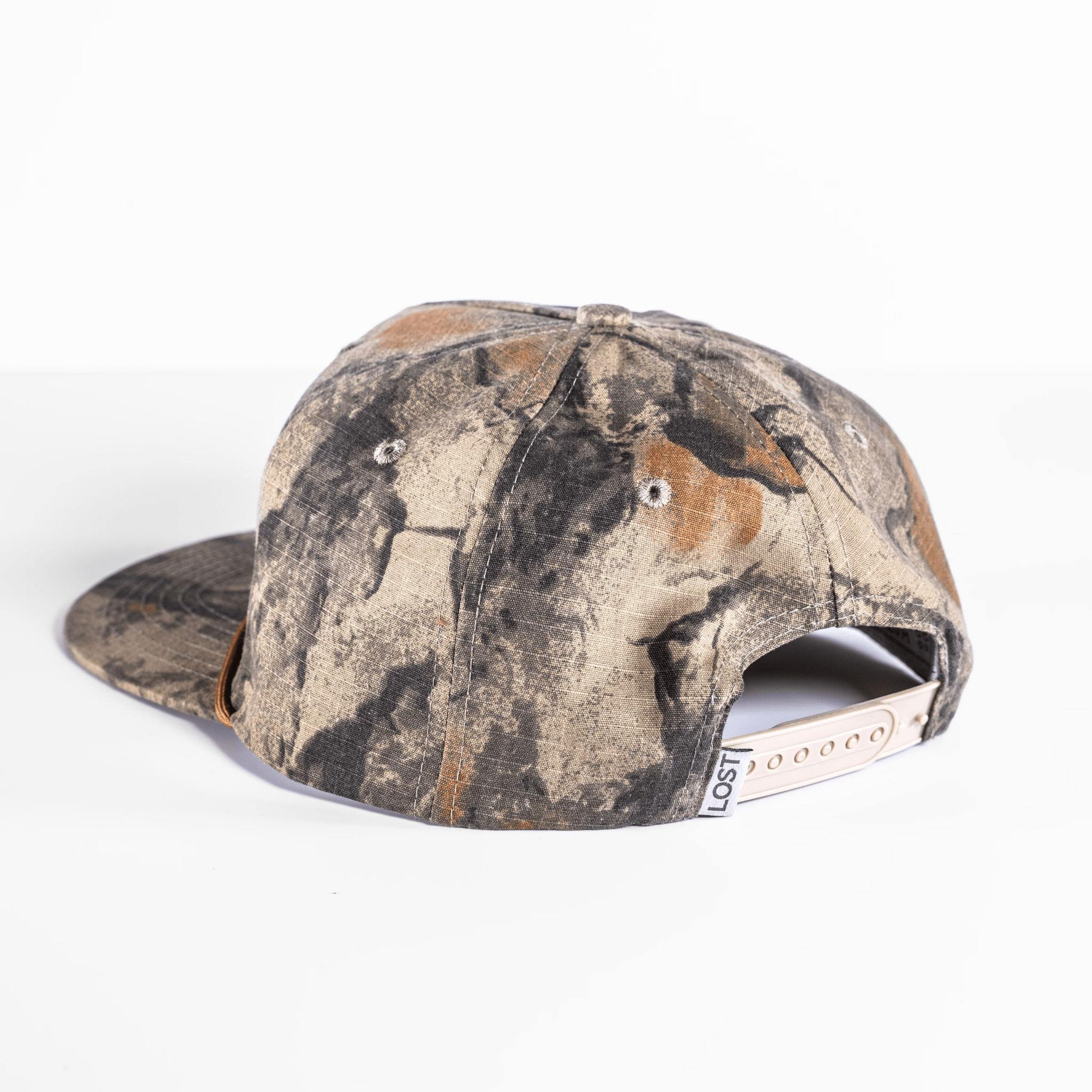 Back view of the Shelter Institute Camo Hat, showcasing a camouflage pattern with a leather patch featuring the Shelter Institute logo and a snapback closure on a white background.