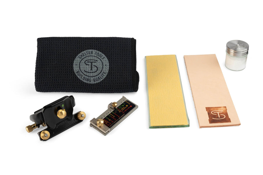 The Shelter Sharpening Kit by Shelter Institute includes a Veritas MKII Honing Guide, black cloth, angle gauge, glass plate with abrasive, leather strop, and small jar, all arranged on a white background.