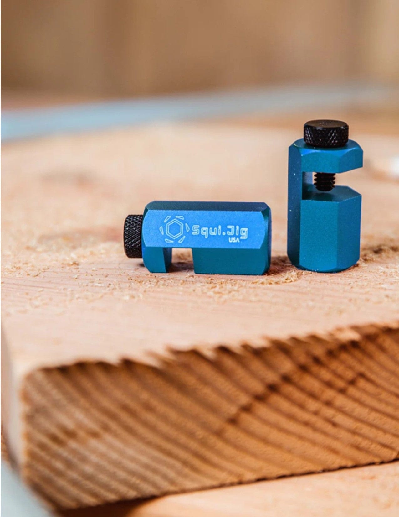 Two small blue Squi.Jig Framing Stair Gauges with black adjustment screws rest on wood. The left gauge lies on its side showing the Squi.Jig branding, while the right stands upright, ready for precise stair layout.