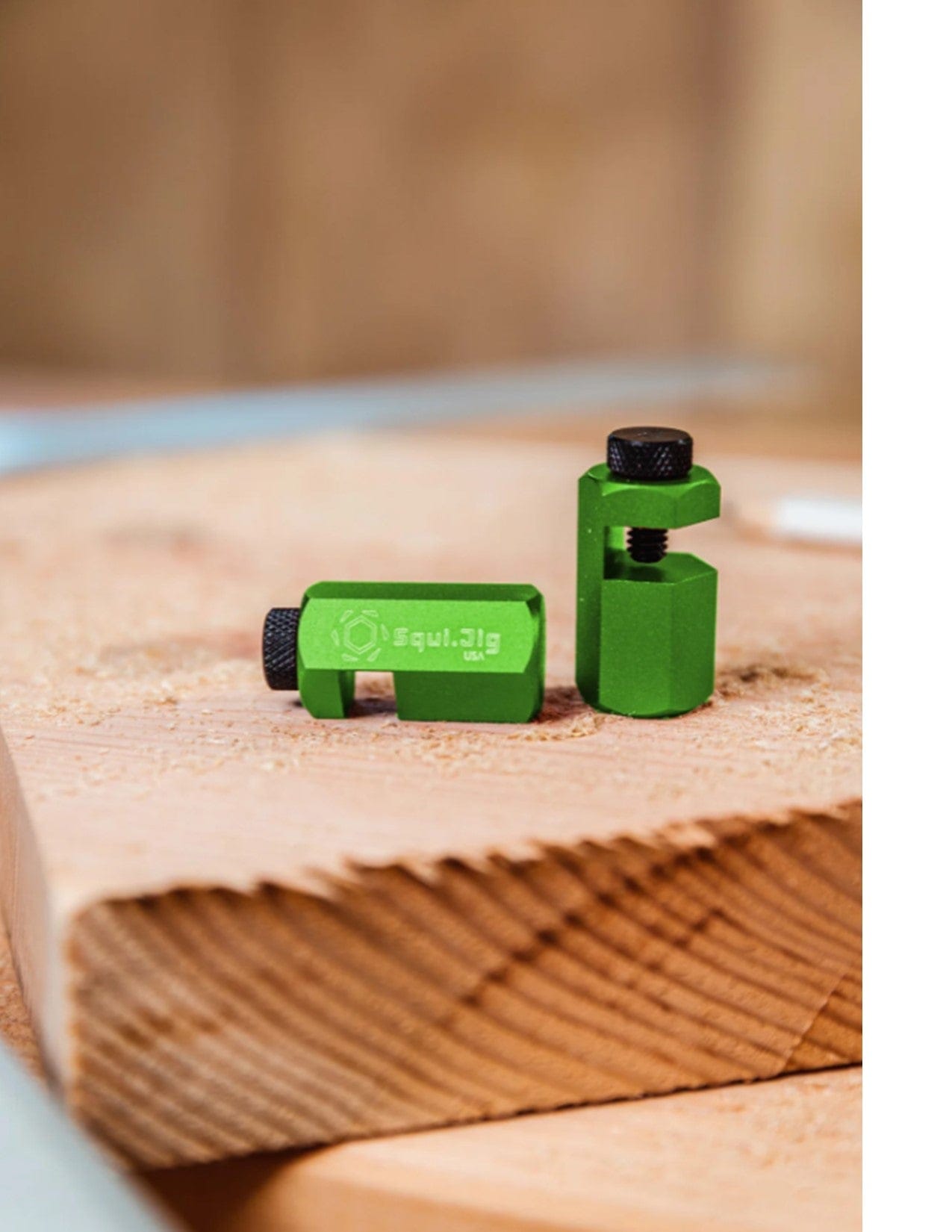 Two small green Squi.Jig Framing Stair Gauge clamps with black screws rest on unfinished wood. Branded Squi.Jig, these are perfect for precise woodworking tasks like stair or rafter layout.