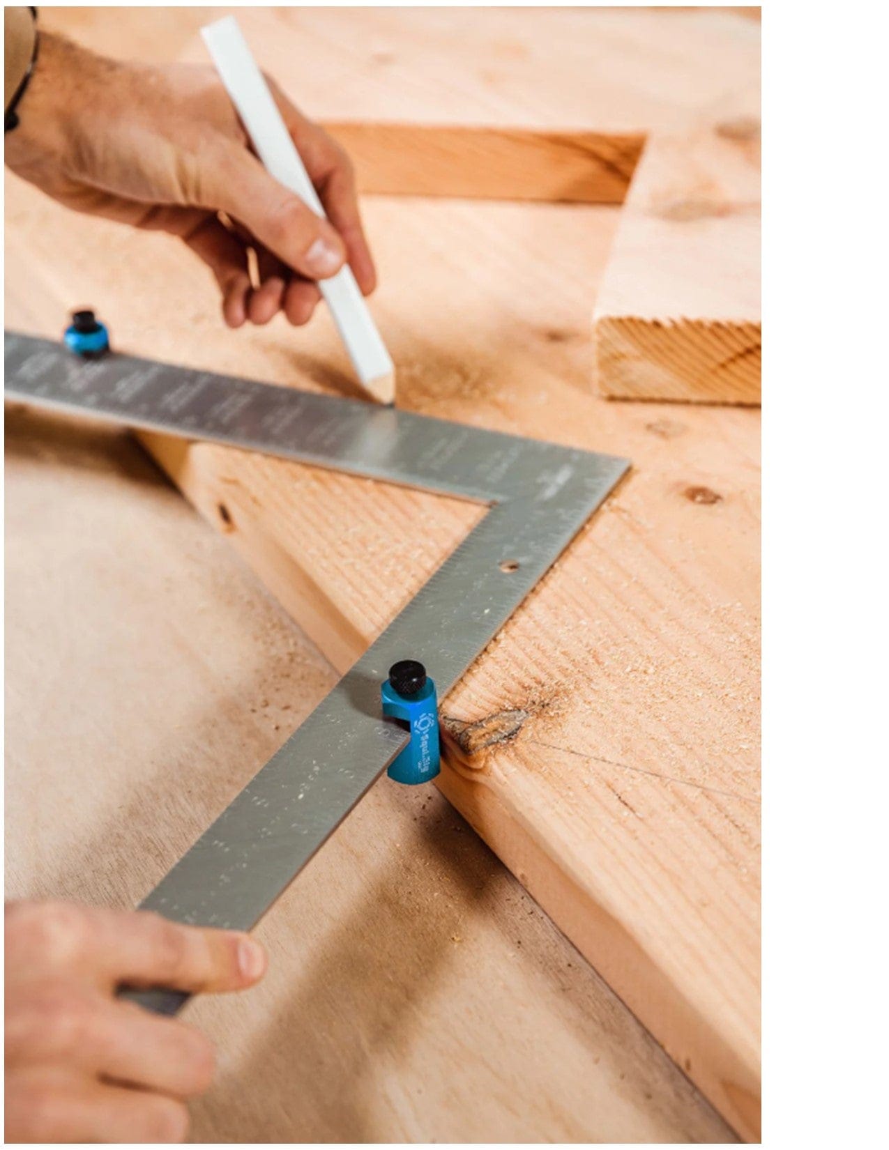 A person uses the Squi.Jig Framing Stair Gauge by Squi.Jig and a white pencil to mark a precise rafter layout on a wooden board in a woodworking workshop.