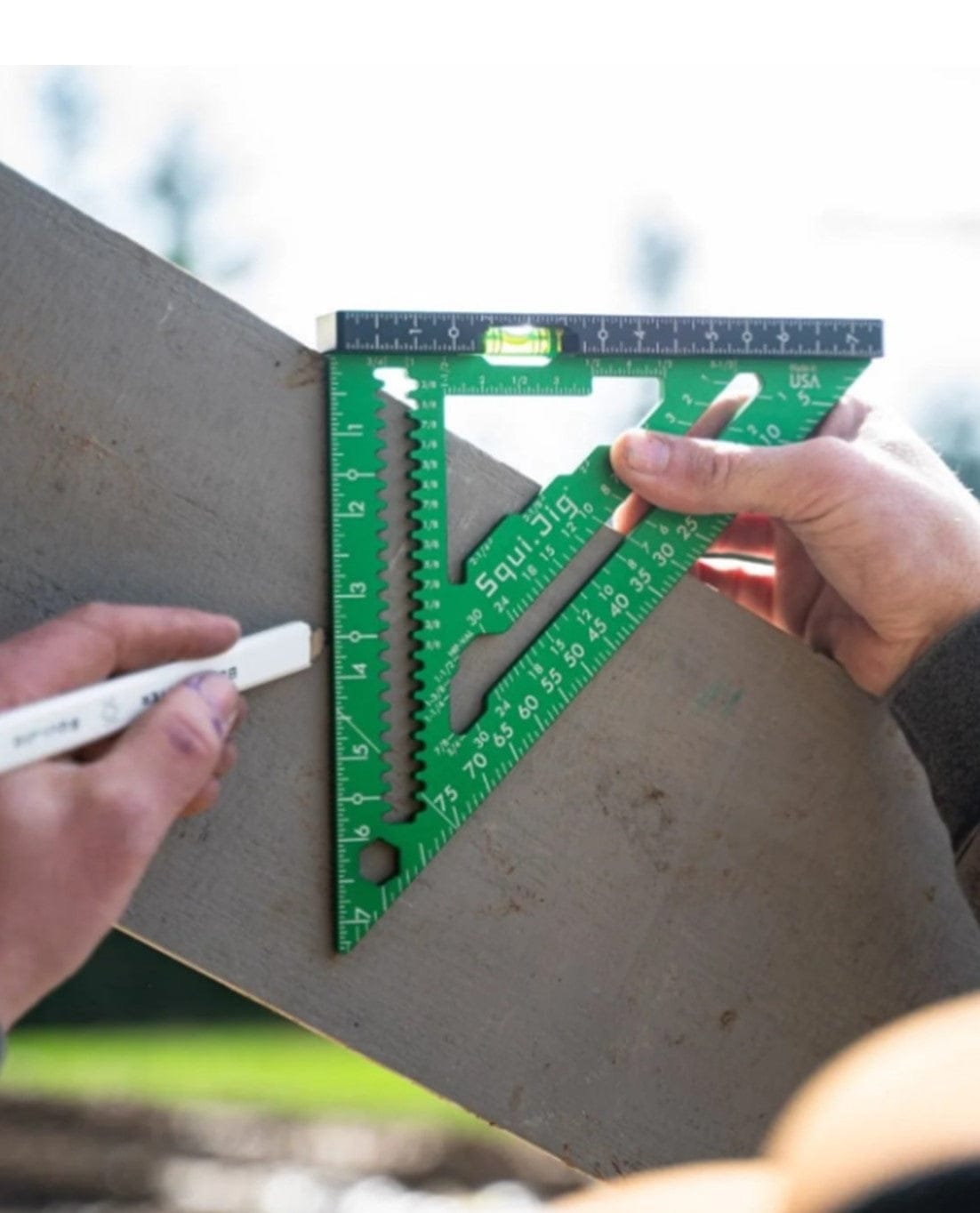 A person marks wood with a white pencil using a green Squi.Jig Fusion 7.5 inch Pro Rafter Square featuring various measurement markings and notches.
