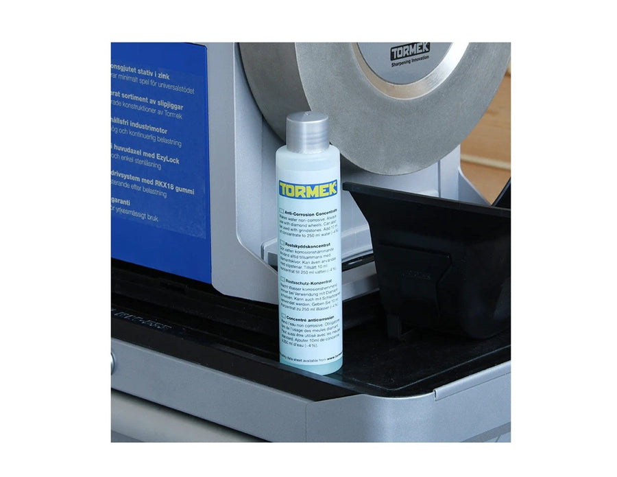 A bottle of TOR Tormek Anti-Corrosion Concentrate, a reliable water trough additive for sharpener corrosion protection, sits on a sharpening machine with its grinding wheel and components visible in the background.