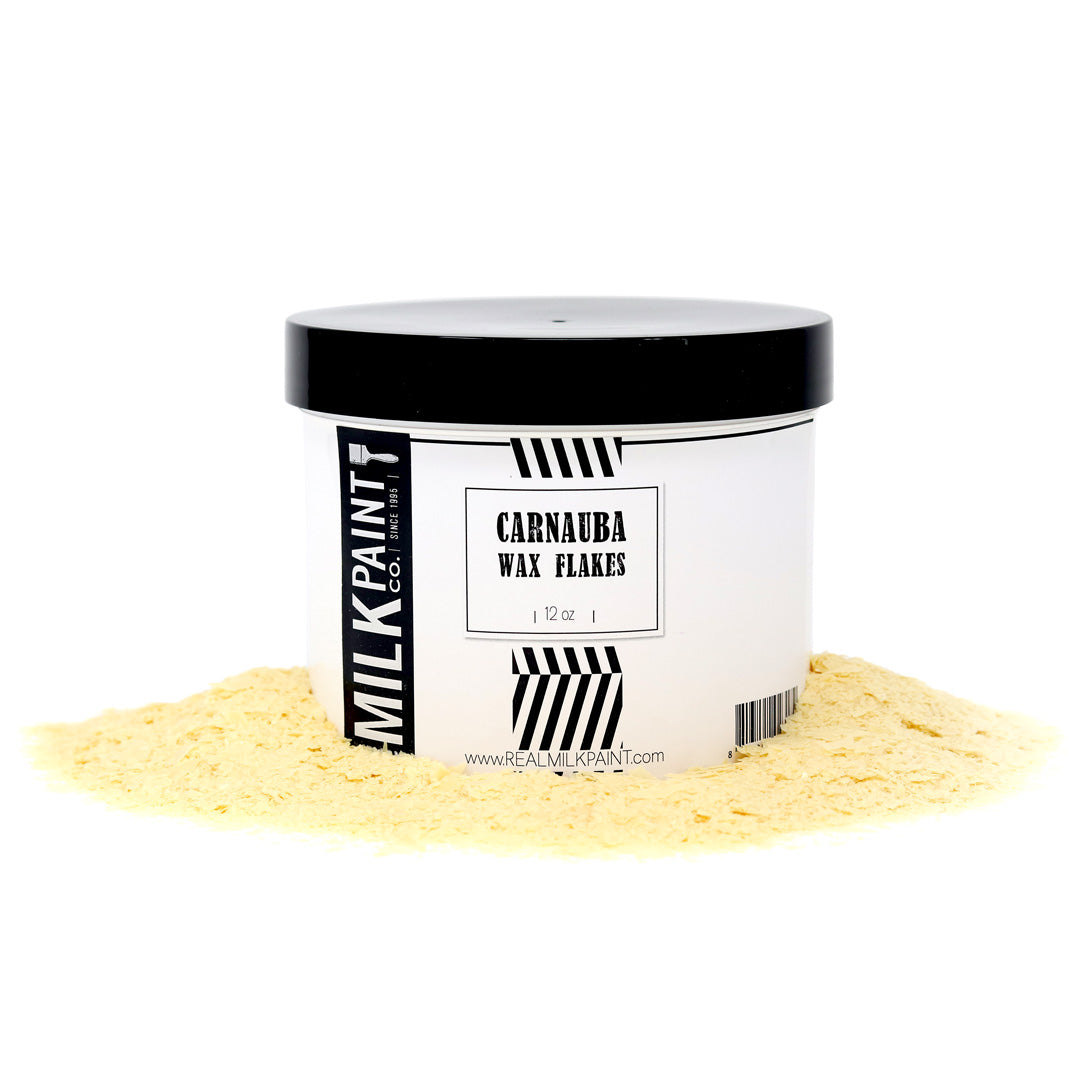 A white container labeled "Milk Paint Carnauba Wax Flakes" by RMP is surrounded by scattered yellow flakes, sourced from the Brazilian Carnauba palm, famous for producing the hardest natural wax.