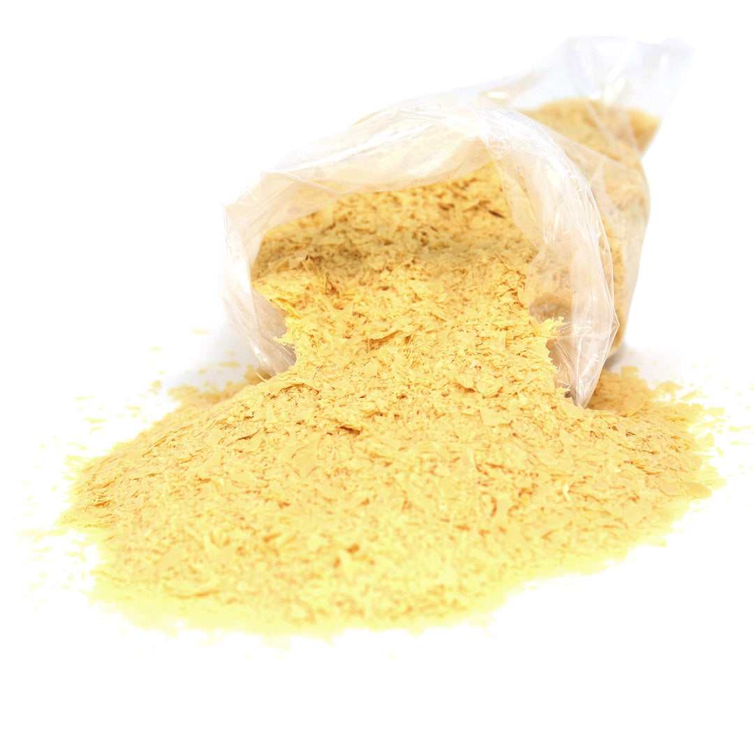 A transparent bag labeled RMP Milk Paint Carnauba Wax Flakes is tipped over, with yellow flakes scattering onto a white surface.