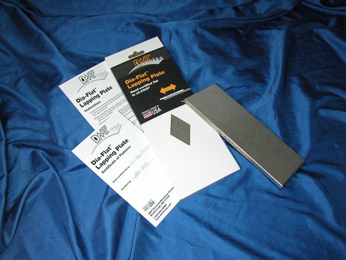 The DMT Dia-Flat Lapping Plate, instructions, a small diamond-shaped piece, and branded packaging with Diamond Hardcoat Technology are displayed on blue fabric.