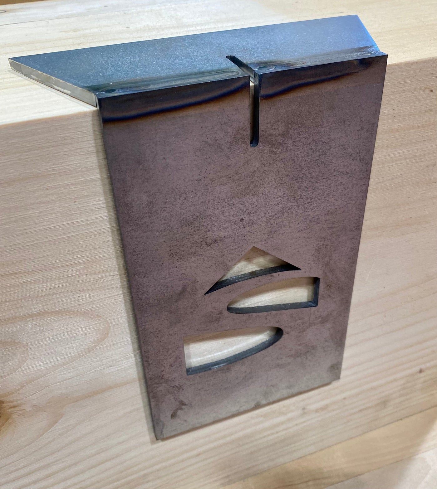 The Timber Frame Dovetail Layout Jig by Engineering Paige Trucks Restoration rests on wood, displaying arrow and wavy line cutouts—ideal for marking dovetail joinery in timber framing projects.