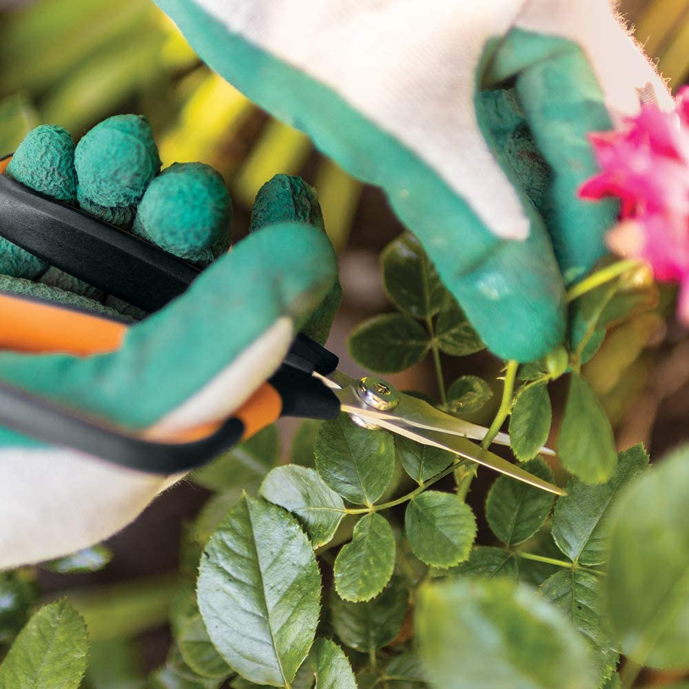A person wearing green and white gloves uses the Fiskars Micro-Tip Pruning Snip by FIS, which features stainless steel blades, to cut a stem from a plant with pink flowers.