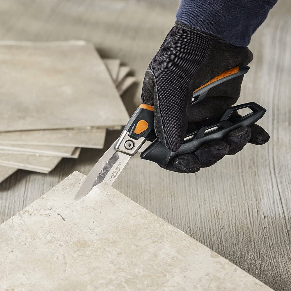 A gloved hand expertly uses FIS PowerArc Utility Snips (8 Inch) to cut through tile, with several tiles in the background. The snips ergonomic design and stainless steel blades ensure precision.