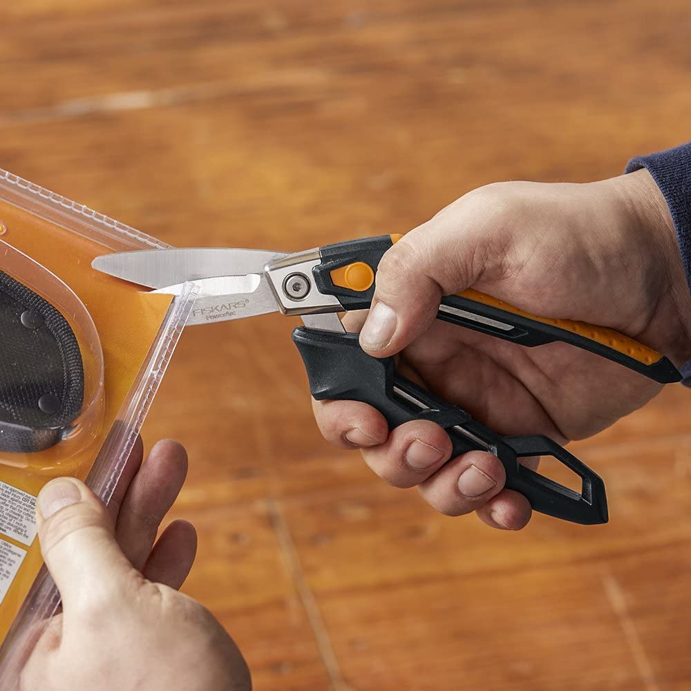 A person is using FIS PowerArc Utility Snips (8 Inch) with stainless steel blades to cut through plastic packaging.