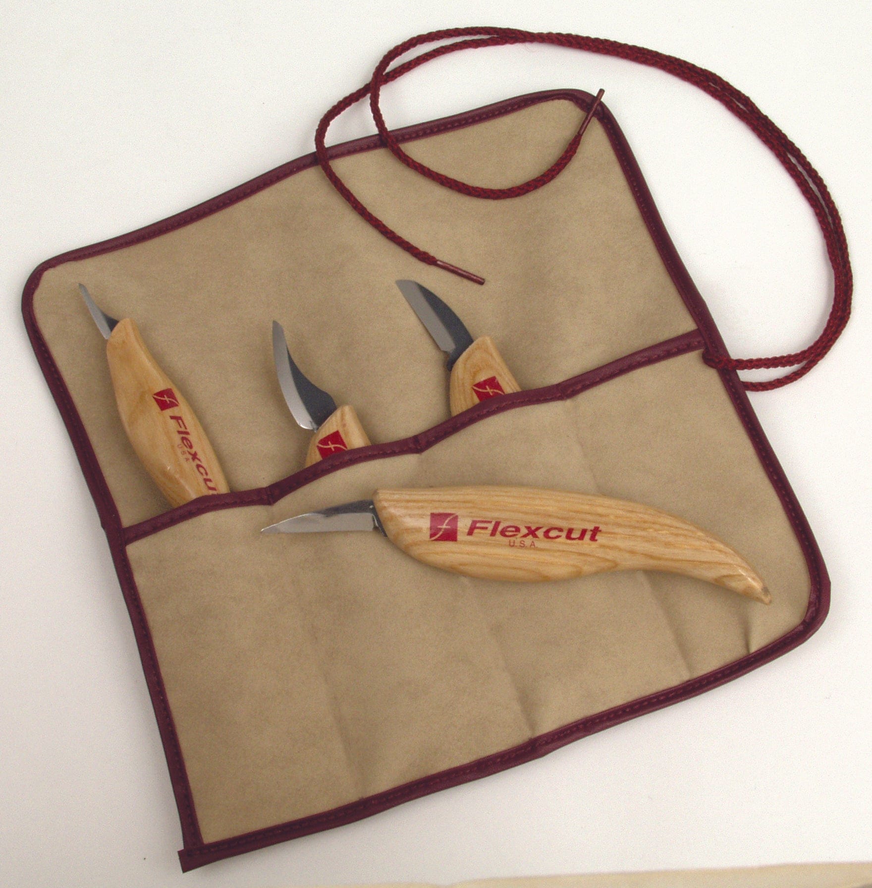 The Flexcut Carving Knife Set 4-Piece by FLE has ergonomic wooden handles and is neatly housed in a tan fabric pouch with a maroon border and cord, featuring razor-sharp knives ideal for wood carving tasks.