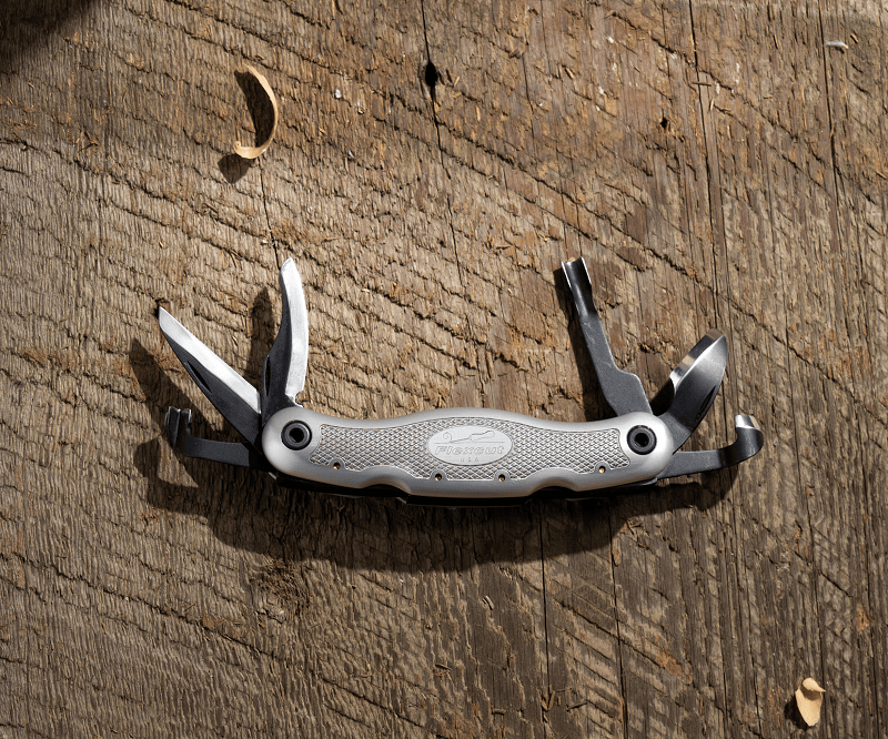 The FLE Carvin Jack 2.0, a versatile woodcarving multi-tool, rests elegantly on a textured wooden surface surrounded by delicate shavings.