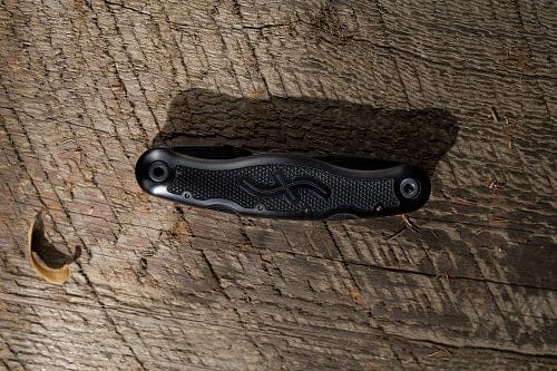 A closed FLE Pocket Jack 2.0 folding pocket knife with a textured black handle sits on a rough wooden surface in natural light.