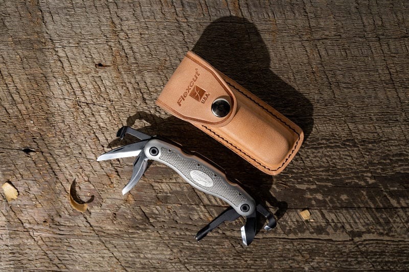 The Carvin Jack 2.0 by FLE, a multifunctional woodcarver's tool with a wooden handle, sits on a wooden surface. A brown leather case nearby adds elegance to this essential folding tool.