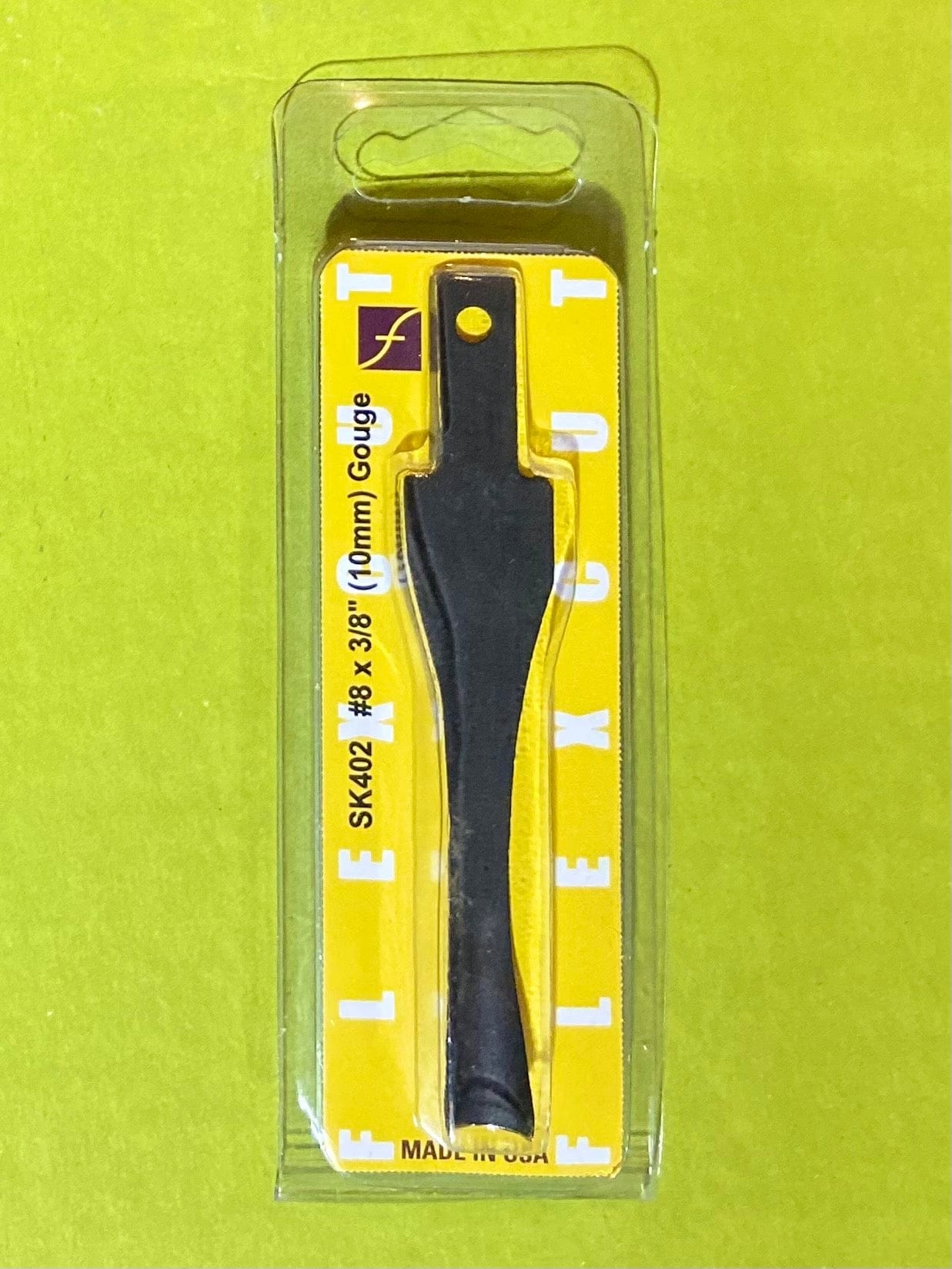 A Flexcut Gouge Blade by FLE is sealed in clear plastic packaging with a bright yellow background. The flat, wide blade features a small mounting hole at the top.