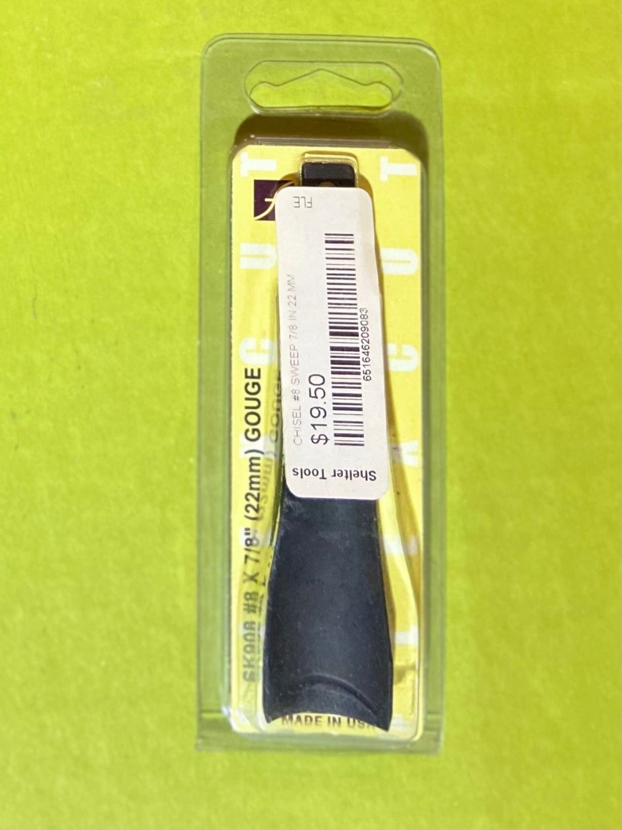 A 22 mm Flexcut Gouge Blade by FLE with a black handle, packaged in plastic and priced at $19.50 (barcode sticker shown), is displayed on a yellow-green surface.
